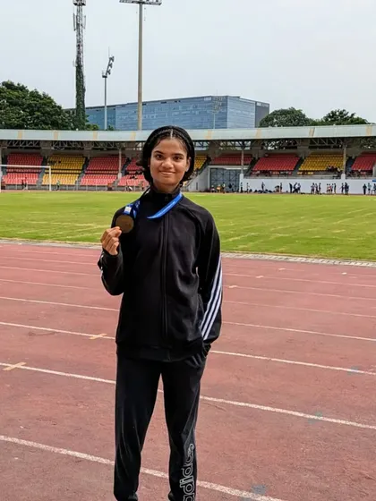 An athlete holding her bronze medal on the track after competing in the 80m hurdles at the junior state meet.