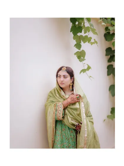 A simple yet elegant full-length portrait of the bride in her beautiful green outfit, set against a clean, white wall.