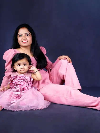 A mother and her daughter, dressed in matching pink outfits, share a quiet moment together against a dark, classic backdrop. A lovely mother-daughter portrait.
