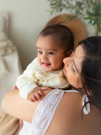A happy 6-month-old baby snuggled safely on her mother's shoulder. This portrait is full of warmth, comfort, and the sweet connection between them.