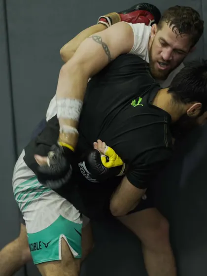 Two fighters working on clinch and takedown techniques against the wall. This is a crucial part of MMA wrestling, blending striking and grappling seamlessly.