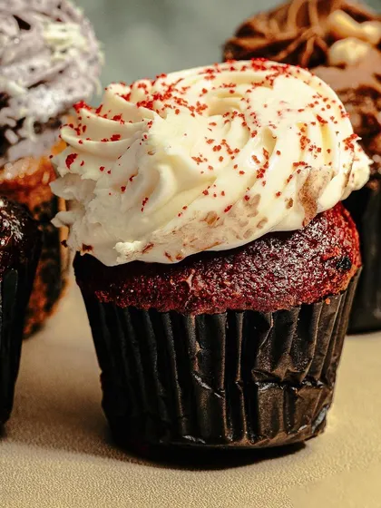 A close-up of a red velvet cupcake, showing the detail of the cream cheese frosting and red sprinkles. We capture every delicious detail to make the food look its best.