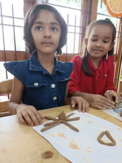 Two campers work together on their clay sculptures, one making a spider and the other a triangle. Collaborative projects like this encourage teamwork and social skills.