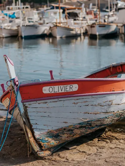 A close-up of a weathered, colorful fishing boat named 'Olivier' beached in St. Tropez. Focusing on small details adds character and authenticity to a destination's story.