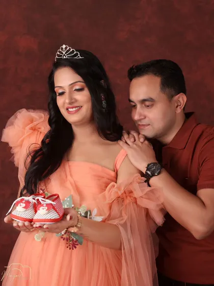 A fairytale in peach tones. The mom-to-be, wearing a delicate tiara, holds up tiny baby shoes as her partner looks on with love, creating a sweet and hopeful portrait.