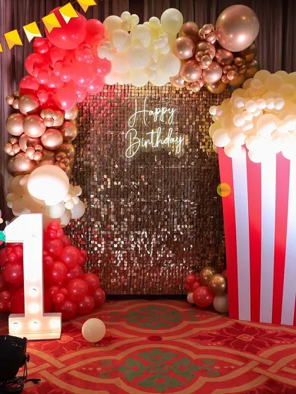 Step right up to the greatest first birthday! This carnival-themed party was a blast to create, featuring a massive popcorn box prop made of balloons, a golden sequin backdrop, and a light-up marquee number '1'.