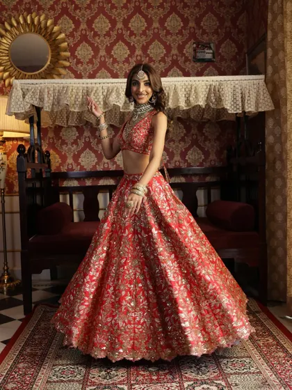 Creating a vintage-inspired bridal portrait. The model is styled in a vibrant red lehenga against a regal, old-world backdrop, evoking a sense of timeless romance and heritage.