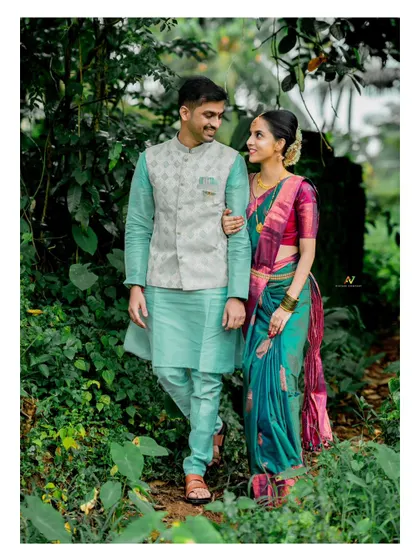 A full-length portrait of a couple walking together in a green, wooded area, capturing a classic and romantic pre-wedding moment.