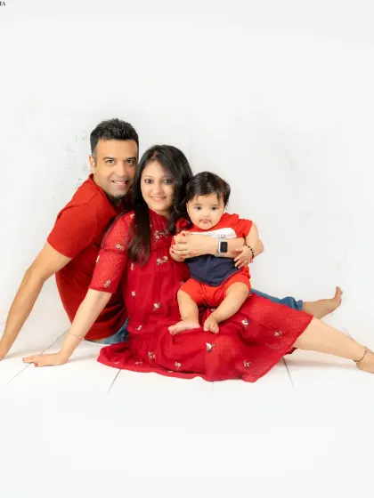 A lovely family portrait with parents and their baby in coordinated red outfits, sitting together in a relaxed pose. It’s a picture of pure family happiness.