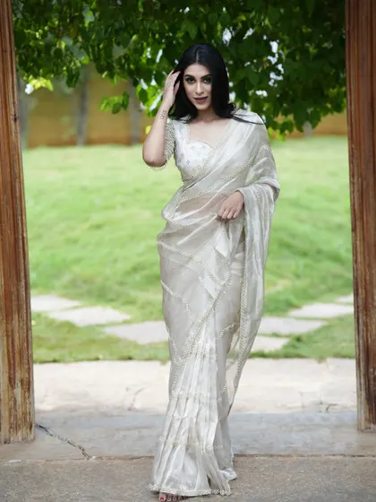 An ethereal white tissue silk saree, adorned with delicate pearl and cutdana embroidery. Paired with a matching embroidered blouse, it's a vision of grace.