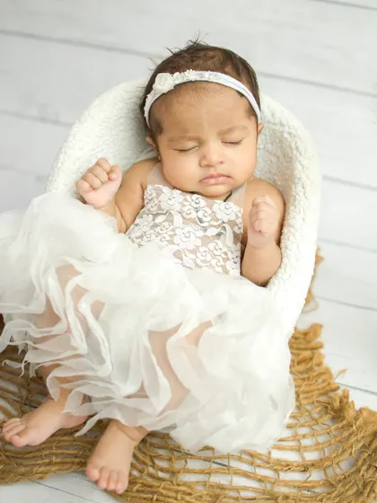 A close-up of the baby in the white lace dress, showing her little fists clenched in sleep.