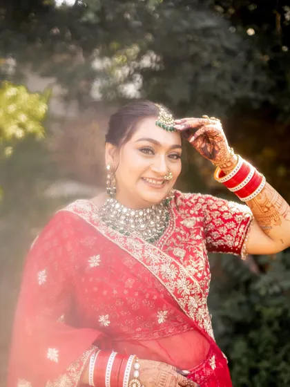 A candid moment of the bride adjusting her maang tikka. The outdoor, natural lighting shows how the dewy makeup looks fresh and luminous.