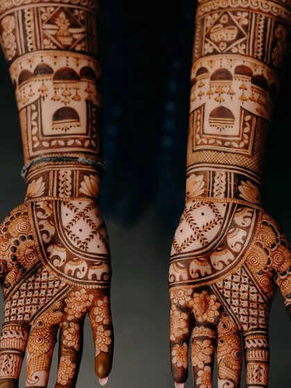 A dark, moody shot of the bridal mehendi, highlighting the intricate patterns and the beautiful contrast against the dark background.