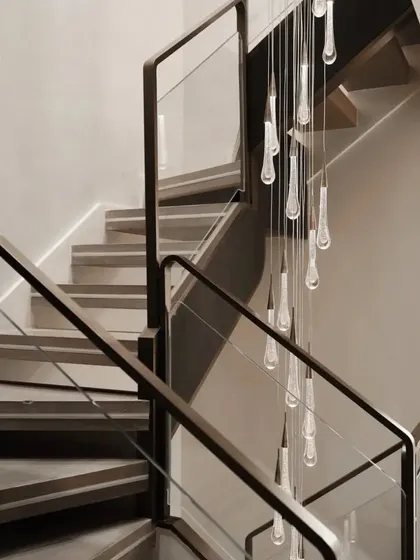 Detail is key in luxury design. This close-up shows a custom-designed staircase featuring clean lines, glass paneling, and a cascading teardrop chandelier that serves as a functional art piece within the home.