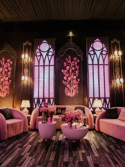 A lounge area with modern pink sofas and gothic-style arched windows. The design is a unique blend of contemporary comfort and dark, romantic drama.