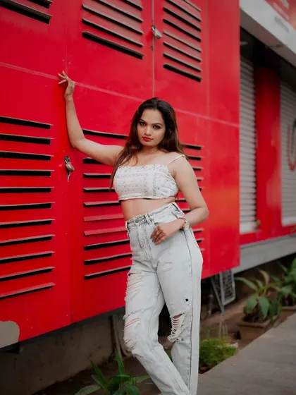 A vibrant street portrait using a bright red wall as a backdrop. The model's casual outfit and confident pose create a bold and eye-catching fashion shot.