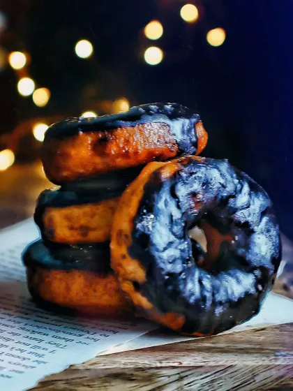 A stack of chocolate-glazed donuts set against a dark background with soft, warm lights. This moody photography style highlights the rich texture of the glaze and creates a cozy, late-night treat vibe.