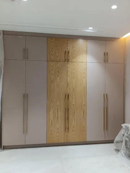 A modern wardrobe design combining a neutral painted finish with a central panel of natural wood veneer. The long brass handles add a touch of sleek elegance.