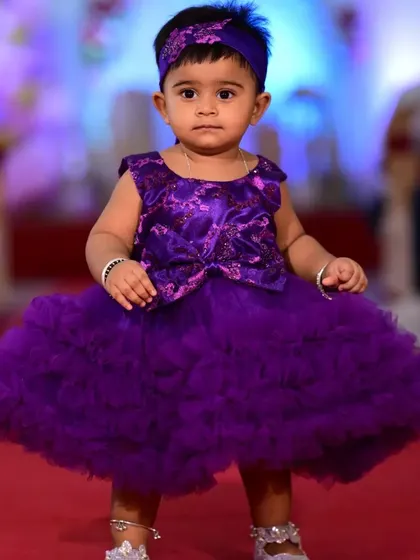 A front-on view of the custom purple ruffled dress, showing the bow detail and the incredible volume of the skirt. This dress is designed to make a statement and comes with a matching headband.