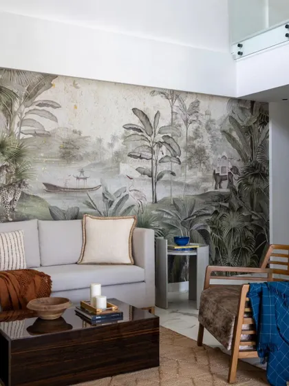 This living room in a Jaipur penthouse features a stunning Ranthambore-inspired wallpaper, creating an immersive escape. The neutral sofa and dark wood coffee table allow the intricate jungle scene to be the star of the room.