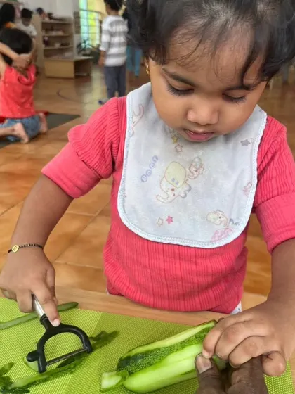 A very young child learns to peel a cucumber. Using child-safe tools, she develops fine motor skills and hand-eye coordination while preparing a healthy snack for herself and her friends.