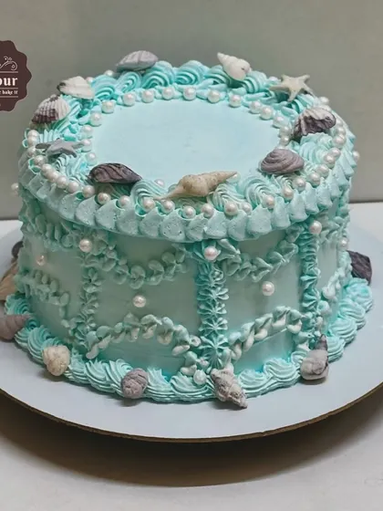 A vintage-style underwater theme cake. The delicate piping work in shades of blue and white creates an elegant, classic look, adorned with edible chocolate seashells.