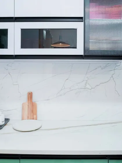 This kitchen features a unique combination of green lower cabinets and white upper cabinets with black-framed glass doors. The white marble countertop and backsplash create a bright, luxurious feel.