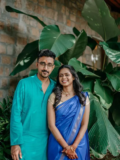 A classic couple portrait against a lush green backdrop. The vibrant colors of their outfits in this South Indian engagement shoot pop beautifully.