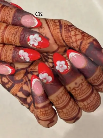 For the bride who loves red. This set features a mix of bold red nails and French tips, all adorned with 3D flowers and pearl centers to match the henna design.