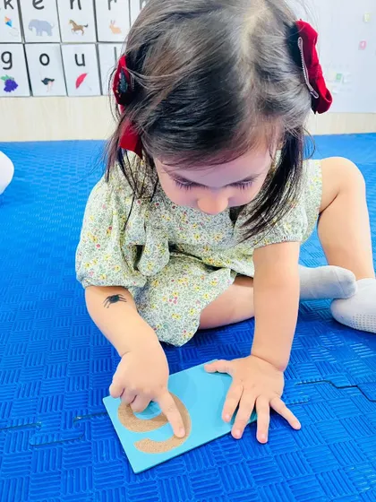 A child traces a sandpaper number "6" with her finger. This tactile experience helps solidify number formation in her memory.