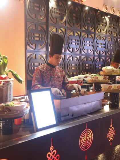 A chef at a Pan-Asian station, set against an ornate, traditional backdrop. We pay close attention to the details of our themed stations to create an authentic and immersive atmosphere.