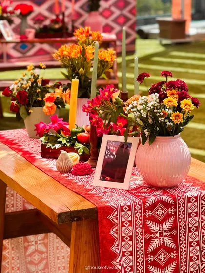 A rustic yet vibrant tablescape featuring a traditional patterned runner, colorful floral arrangements in a pink vase, and tall candles, perfect for a lively daytime event.
