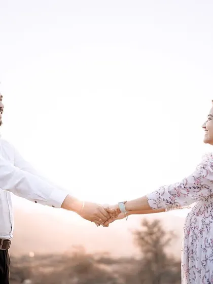 A classic pre-wedding pose, holding hands and looking at each other. The soft sunset light creates a romantic and dreamy atmosphere.