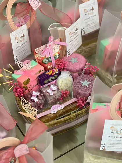 A fully assembled basket-style announcement hamper, overflowing with pink and purple treats and decorated with delicate butterflies.