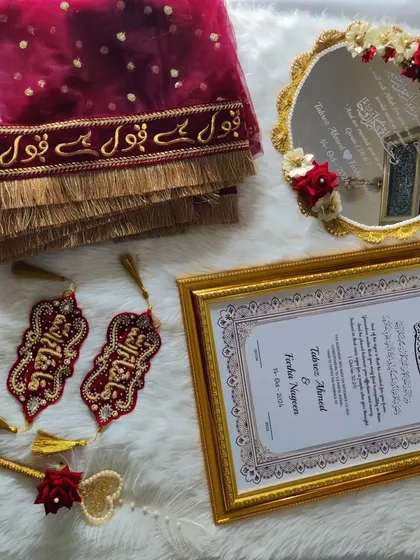 A different arrangement of the red and gold Nikah set. This view highlights the intricate embroidery on the Iman Zamin and the delicate floral work on the Muh Dikhaye mirror.