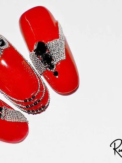 A bold and luxurious design featuring bright red nails adorned with intricate black and silver crystal jewelry.