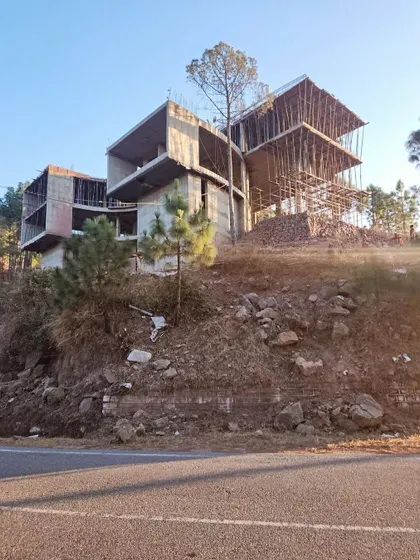 A view of the hillside home from the road below, highlighting its commanding presence and integration with the natural contours of the land. The scaffolding hints at the multi-level design taking shape.