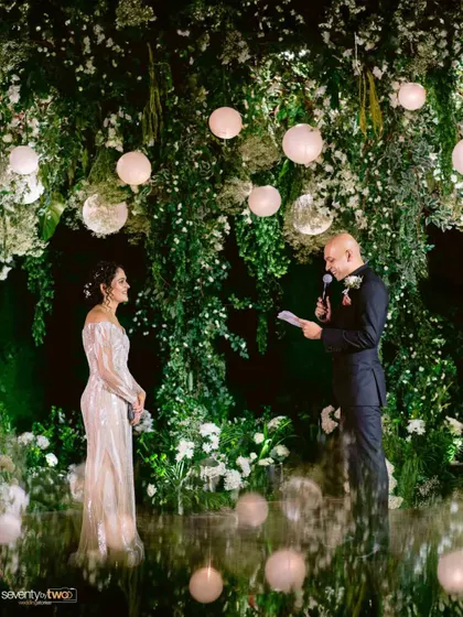 The groom reads his vows to his bride against a stunning backdrop of hanging greenery and glowing orbs, a magical and romantic setting.