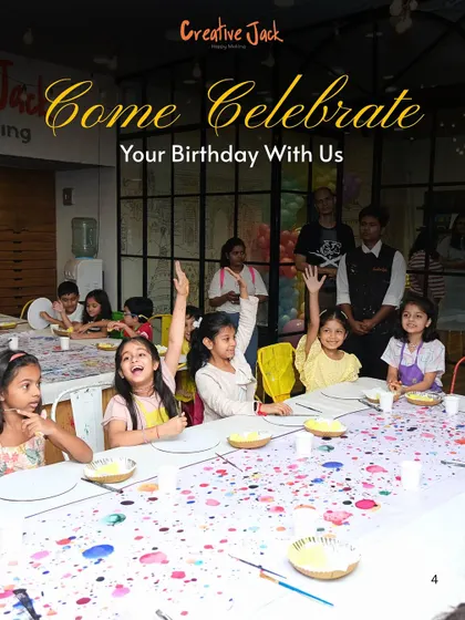A group of excited children raises their hands at a paint-splattered table during a birthday party, ready for the next fun art activity.