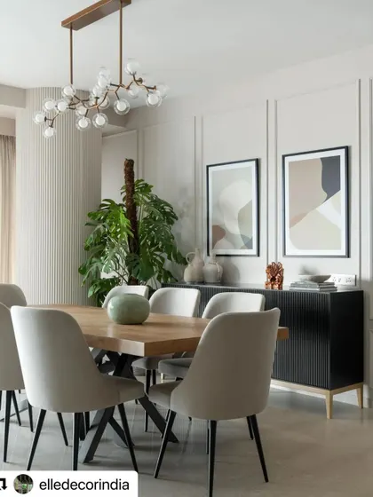 The dining area in the Neutral Chic home is defined by a modern branching chandelier and a dark wood credenza. The space is part of an open-plan layout, connected seamlessly to the living area.