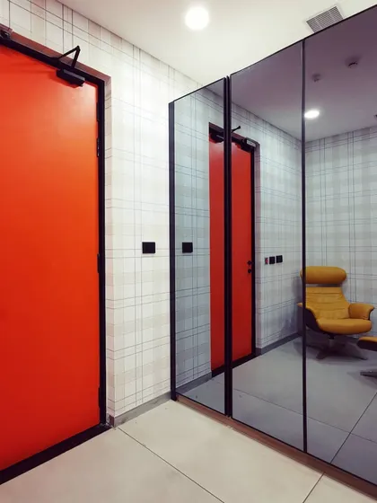 A design detail showing a bold orange door reflected in a mirrored wall, which visually expands the space and creates a dynamic interplay of color and reflection.