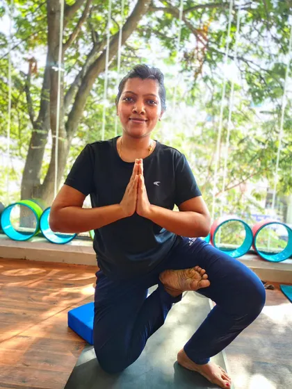A student holds a kneeling balance pose with hands in prayer, demonstrating focus and stability.