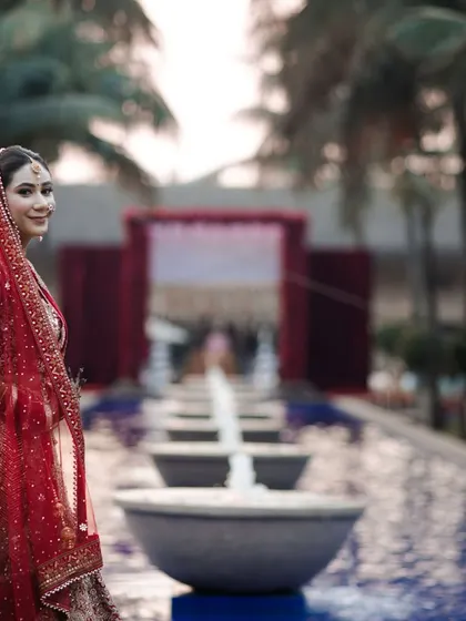 A stunning portrait of the bride in her red lehenga, with the wedding venue in the background. The composition and lighting are planned to create these breathtaking, magazine-worthy shots.
