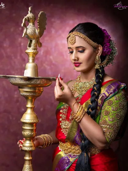 A traditional South Indian bridal look featuring a red and green silk saree, complete with a long braid, temple jewelry, and a hand-embroidered blouse.