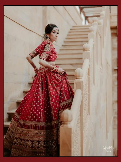 A stunning bridal portrait of Sonakshi on the steps of Suryagarh, Jaisalmer, her red lehenga a vibrant contrast to the sandstone.