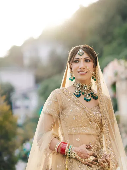 A beautiful, sun-kissed portrait of the bride, with the soft light highlighting her features and the stunning green and gold jewelry she wears.