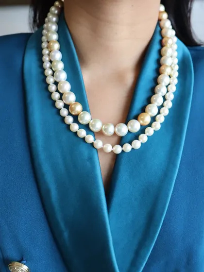 A close-up of the multi-strand pearl necklace, showcasing the beautiful gradient of sizes and the warm tones of the South Sea pearls mixed with the classic white Japanese pearls.