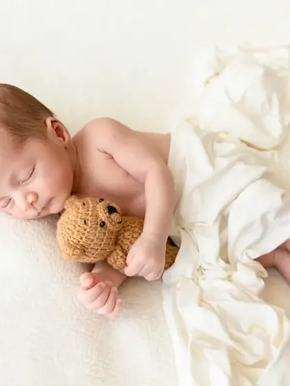 A sleeping newborn cuddles a small teddy bear, a timeless pose that highlights their innocence and tiny size.