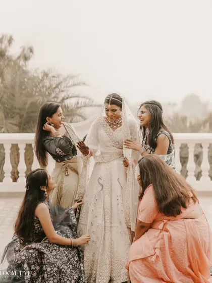 The bride shares a laugh with her bridesmaids, who are all admiring her beautiful white lehenga.