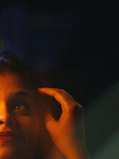 An artistic close-up of a woman's face illuminated by a warm, golden light against a dark background. The abstract light flares add a creative and mysterious element to this low-light portrait.